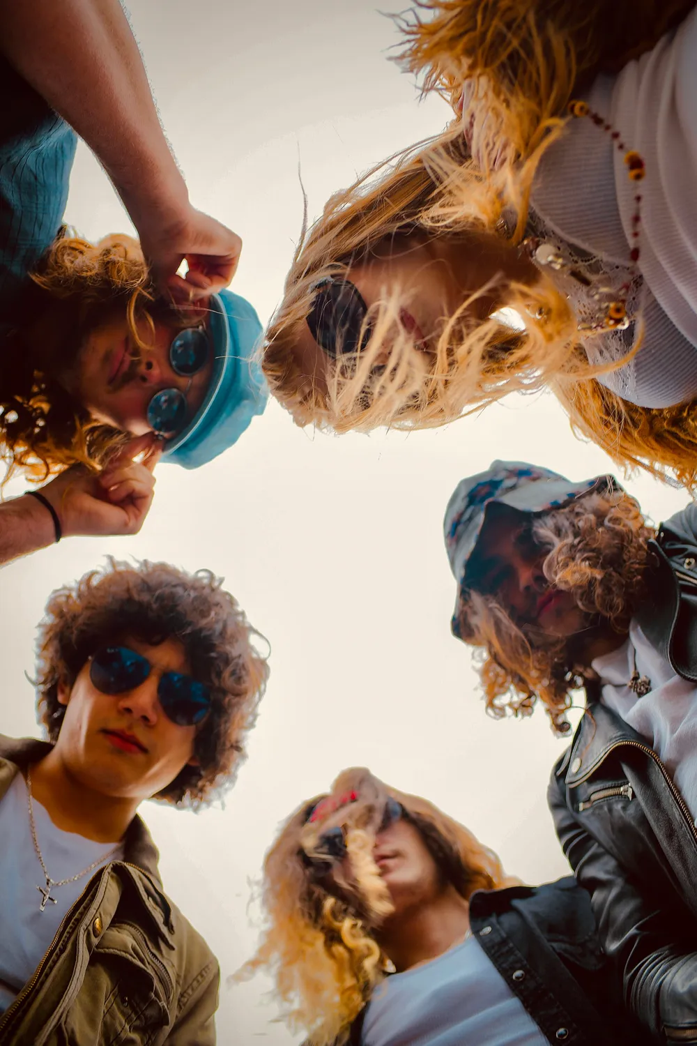 All five members photographed from directly above, standing in a circle and looking up into the lens, one of them reaching a hand toward the camera